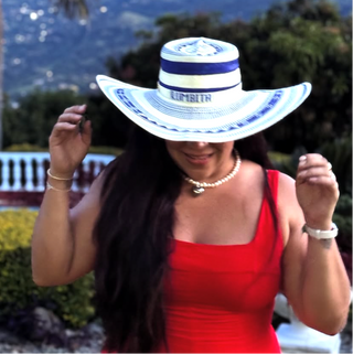 Woman wearing a large white sun hat with blue band outdoors, palm tree and mountains in the background